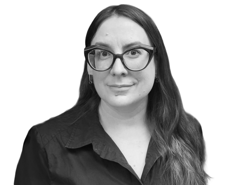 Portrait of a woman wearing large rectangular glasses and a dark button-down shirt, facing the camera with a neutral expression.